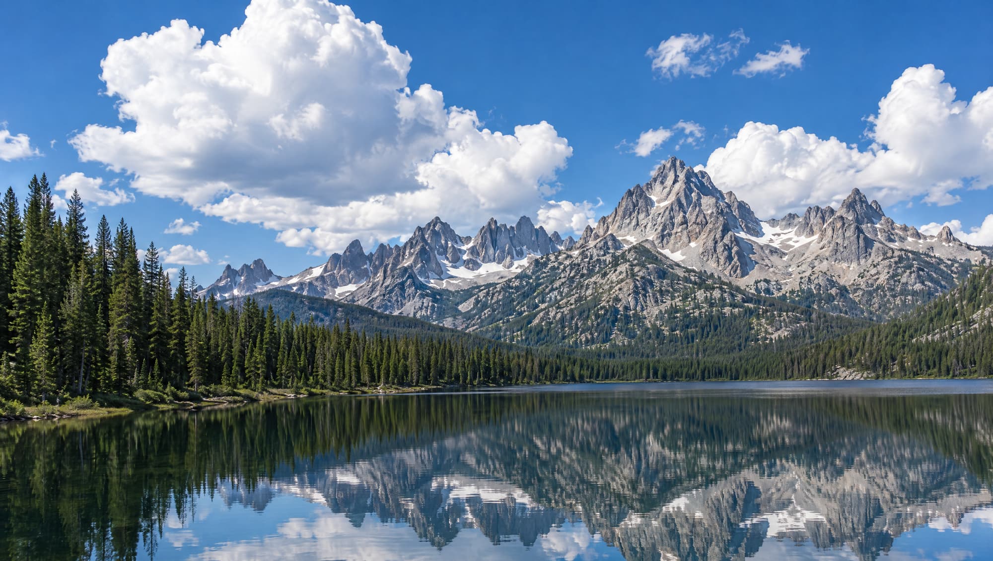 The Sawtooth Mountains of Idaho reflected in a calm alpine lake under white clouds